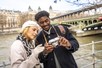 Young multiracial travelers enjoying a romantic city trip to paris, standing by the seine river and
