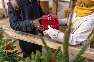 Man handing wrapped red christmas gifts to partner at an outdoor winter market, festive holiday