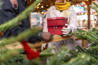 Diverse couple exchanging stack of red gift boxes, celebrating the holiday season at an outdoor