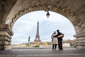 Couple stands embraced on pont de bir hakeim, framed by an ancient archway, observing the eiffel