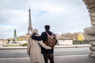 Adult black man and white woman embracing, looking at the iconic eiffel tower and cityscape of