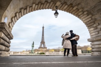 Loving couple embraces under an arched bridge in paris, taking a selfie with the eiffel tower in