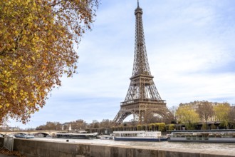 Eiffel tower rising beside the seine as tour boats glide past golden autumn trees and classic