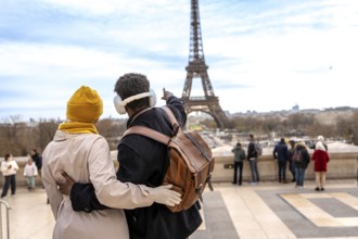 Young couple embracing and looking at the eiffel tower, the man pointing towards the landmark while