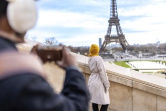 Tourist couple in paris enjoying the view as one photographs the eiffel tower and cityscape with a