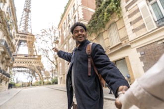 Happy young man of african descent leads his partner by the hand, pointing toward the eiffel tower