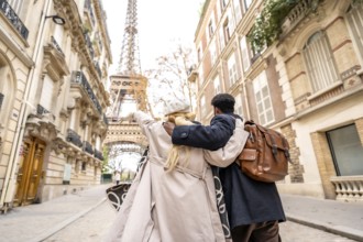 Happy traveling couple embracing as they walk down a cobblestone paris street, pointing toward the