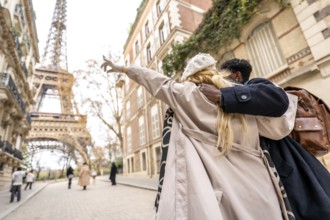 Young diverse couple embracing on a parisian street, with the woman pointing towards the distant