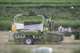 Agricultural machine round baler wraps hay bales in a field, Osnabrücker Land, Lower Saxony,