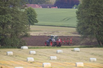 A tractor working in the field, surrounded by green fields and round bales of hay bales in a rural