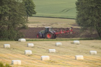 A tractor plows a field surrounded by hay bales and trees in an agricultural scene, Osnabrücker