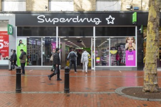 Shoppers entering through doorway entrance of Superdrug shop in town centre of Reading, Berkshire,