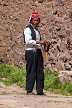 Man wearing a red cap and traditional clothing walks along a stone wall, The knitting men on