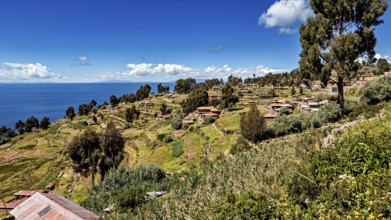 Village with huts on a hill surrounded by green fields and a blue lake under clear skies, the