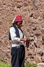 Close-up of a man wearing a red cap and traditional clothes on a stone wall, The knitting men on