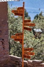 An orange signpost with several international cities and distances in front of a stone wall in a