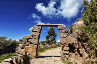 A rectangular stone arch under a cloudy sky, with a path that leads into nature, stone gates on