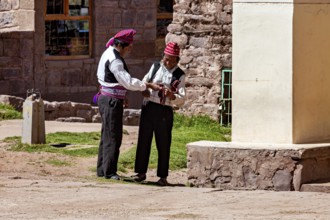 Two men in traditional dress talk next to a stone wall, The Knitting Men on Taquile Island in Lake