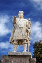 Stone statue of a warrior with a raised hand against a blue sky, Great Inca monument on Taquile