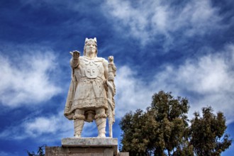 Stone statue of a warrior against a cloudy, blue sky, Great Inca monument on Taquile Island in Lake