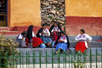 Group of woman in colorful traditional clothing sit on stairs and talk vividly, the woman on