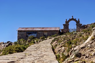 Stone house with archway along a path under a blue sky, stone gates on Taquile Island in Lake