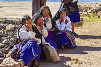 Elderly woman in traditional clothing sitting in the sun on a stone wall, the woman on Taquile