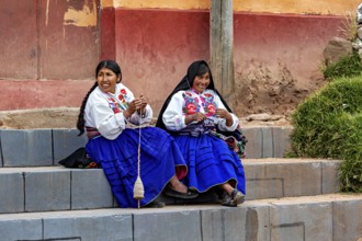Two woman in traditional clothing sit on stairs and spin by hand, the woman on Taquile Island in