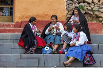 Women and children in traditional clothing sit on steps and interact with each other, the woman on