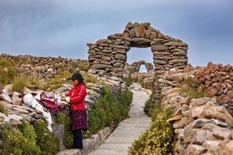 Woman next to clothes on traditional path with stone walls, stone gates on Taquile Island in Lake