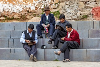 Four men in traditional clothing sit relaxed on stone steps in an urban setting, men sit together