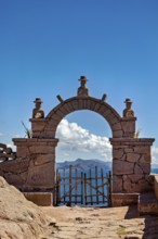 A stone archway with decorations that opens up to a vast mountain panorama under a blue sky, stone