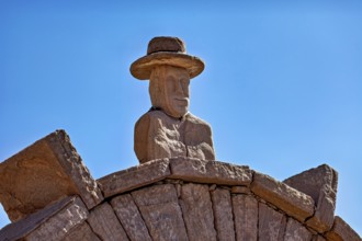 Stone bust with hat on an archway, artfully designed against a clear blue sky, stone gates on the