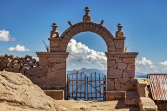 A traditional stone arch with wooden slats stands in front of a distant mountain landscape under