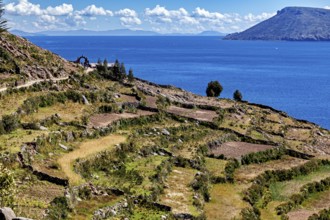 Terraced fields stretch down to a clear blue lake, framed by stone arches and hills, the