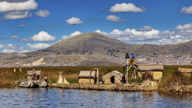 Reed huts and lakeside observation tower with mountains in the background under blue sky, The