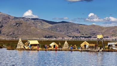 People and reed huts on the shore of a lake with mountains in the background under a clear sky, The