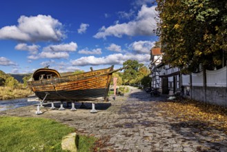Rustic wooden boat on supports on a paved road next to a half-timbered house in autumn, the port of