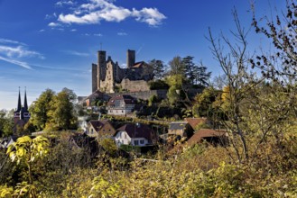 Castle above a village with a church, surrounded by autumn trees under a blue sky, Hanstein Castle
