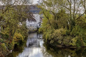 A picturesque village with half-timbered houses on a quiet river, surrounded by autumn trees,