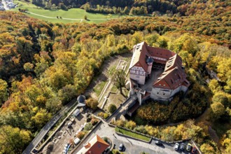 Castle with red tiled roofs, surrounded by autumn-coloured forest landscape, from a bird's eye