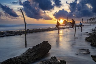 Fishermen fish at sea at sunset, the clouds are dramatically illuminated, Koggala beach with stilt