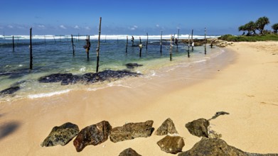 Quiet beach with clear waves and wooden poles under blue skies, Koggala beach with stilt fishermen