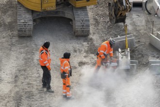 Construction workers in protective clothing work with machines on a dusty construction site,