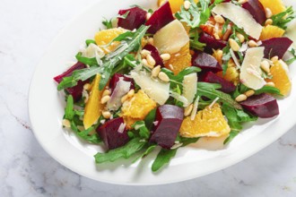 A salad made with chunks of beet, orange slices, and arugula. It is topped with cheese shavings and