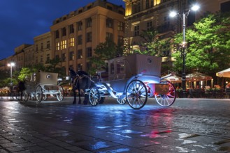 Waiting horse-drawn carriages at the market square at night, Krakow, Poland