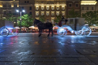 Waiting horse-drawn carriages at the market square at night, Krakow, Poland