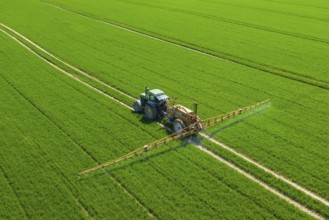 Aerial view over agricultural trailed field sprayer pulled by tractor spraying crop on farmland,