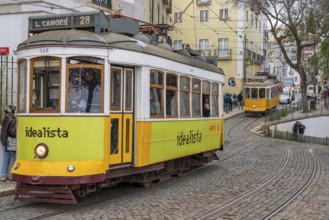 Traditional vintage yellow trams on tram line 28 climbing steep cobbled street in the capital city