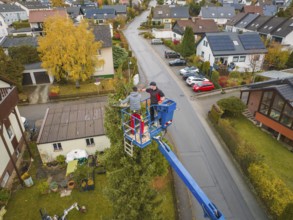 Worker in a lift in an urban area with residential buildings and autumn trees, tree work,